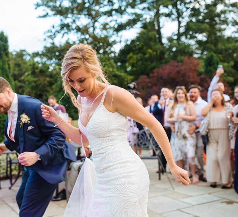 Bride in a beaded wedding dress and groom in a navy suit perform a surprise first choreographed wedding dance for their guests 