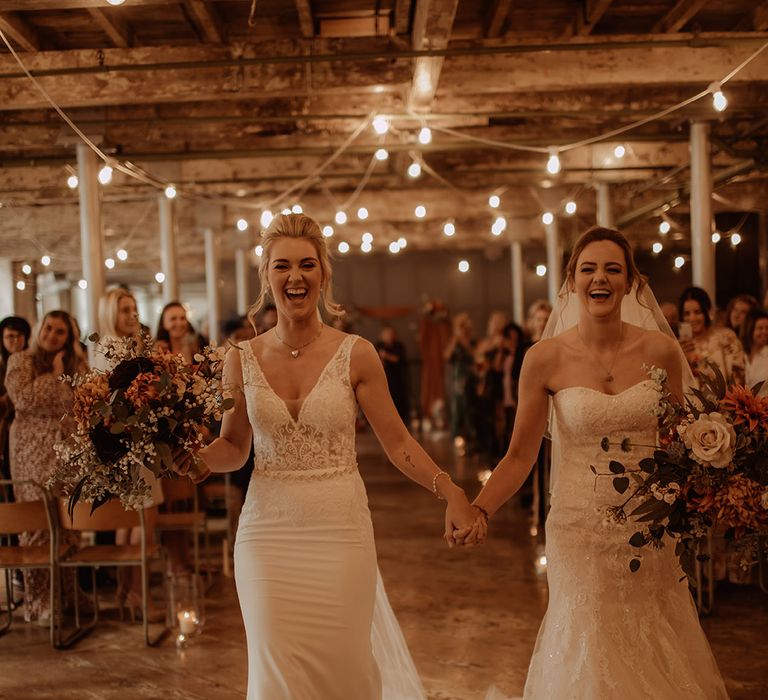 Brides hold hands with one another as they walk together on their wedding day