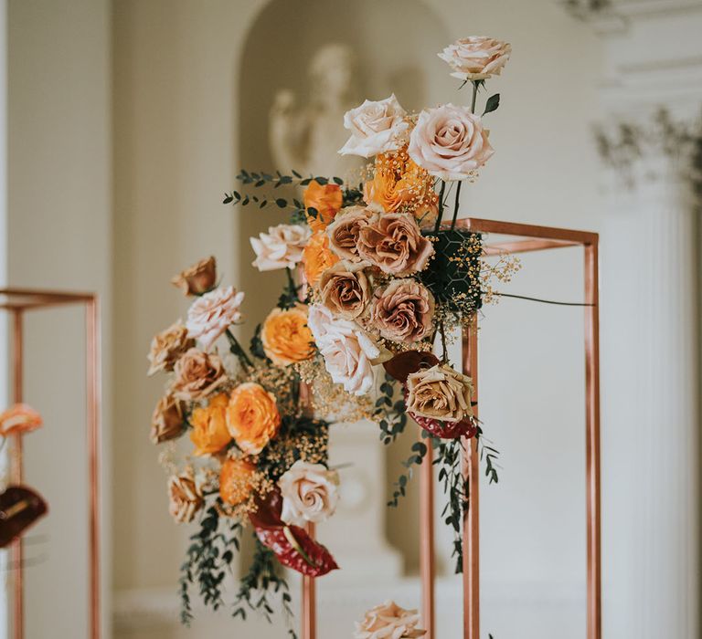 Orange, pink and peach wedding flowers on a metal stand 