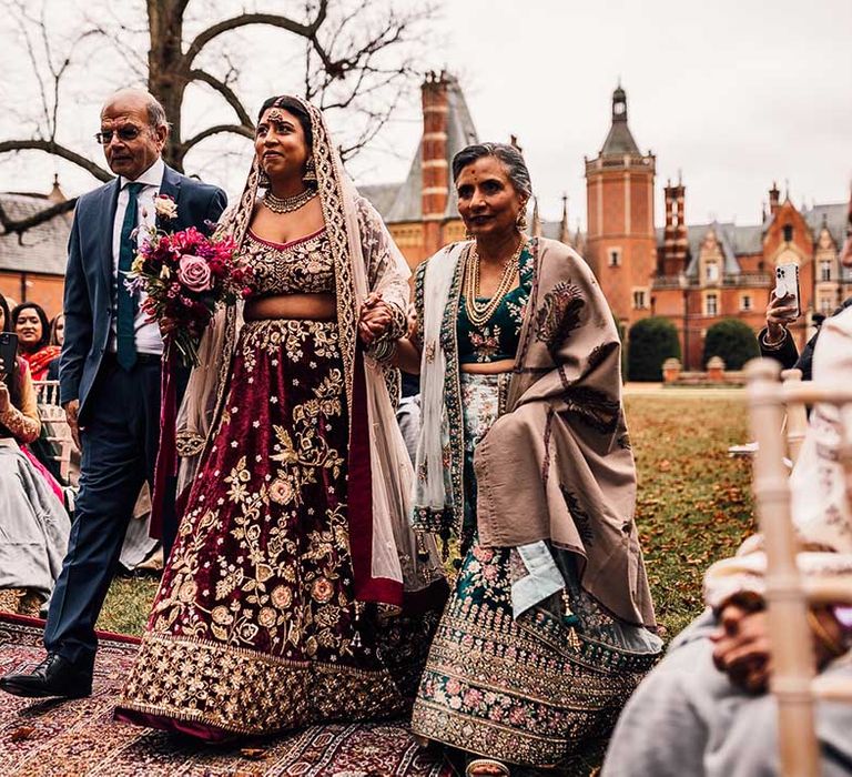 Mother and Father hold their daughters arm walking her down the aisle 