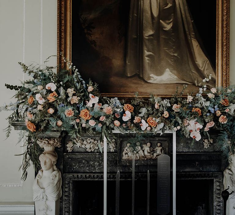 dramatic fireplace floral arrangement with cafe au late roses, orchids and foliage and an acrylic seating chart hanging on a metal frame 