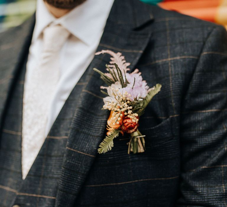 Groom in check suit three piece suit and pink tie wears purple and orange floral buttonhole