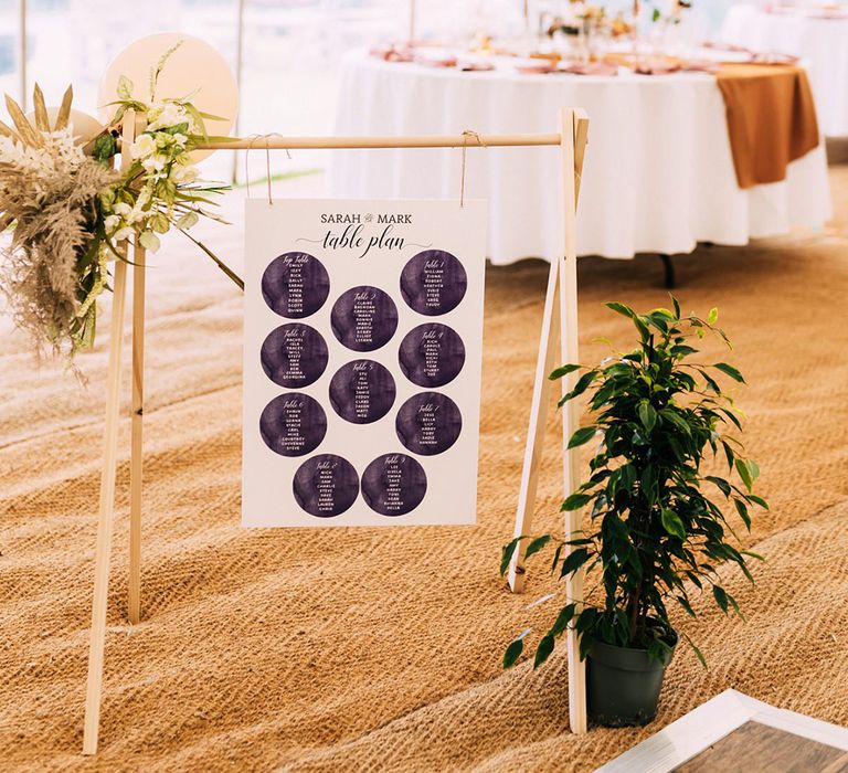 Hanging seating chart with circular patterns on wooden stand with balloons and flower decor 