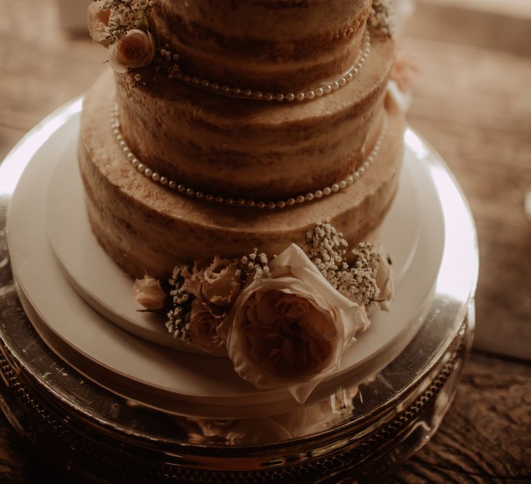 Naked rustic wedding cake complete with florals and pearl decor dotted around the sides 