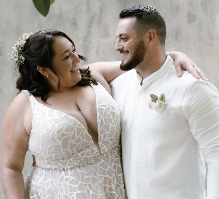 Bride in v-neck illusion geometric wedding dress with wedding guest in white linen shirt and white flower buttonhole