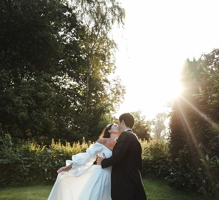 Bride in princess style wedding dress kisses groom in lush green landscape