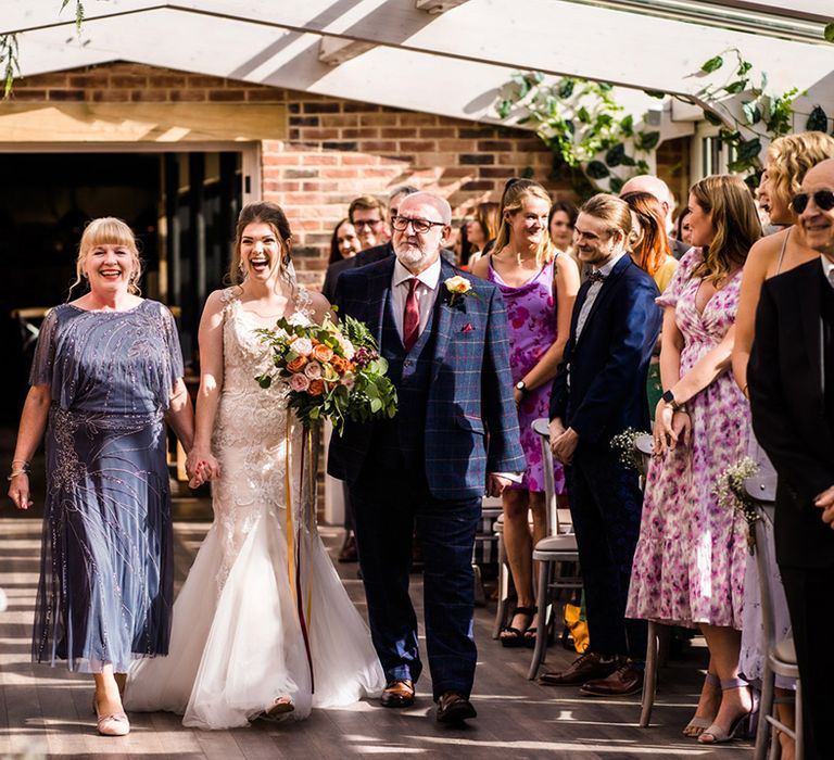 Bride in lace mermaid skirt wedding dress is walked down the aisle by her parents 