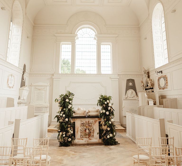 All white ceremony room with marble altar and statues with column flower displays including white roses