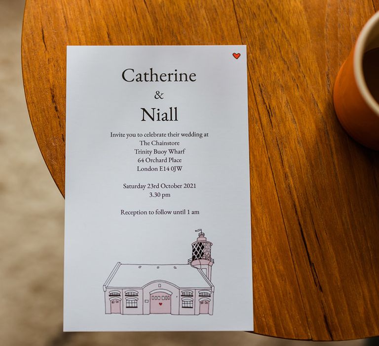 Wedding invitation with pink drawing of wedding venue with red heart in right corner 