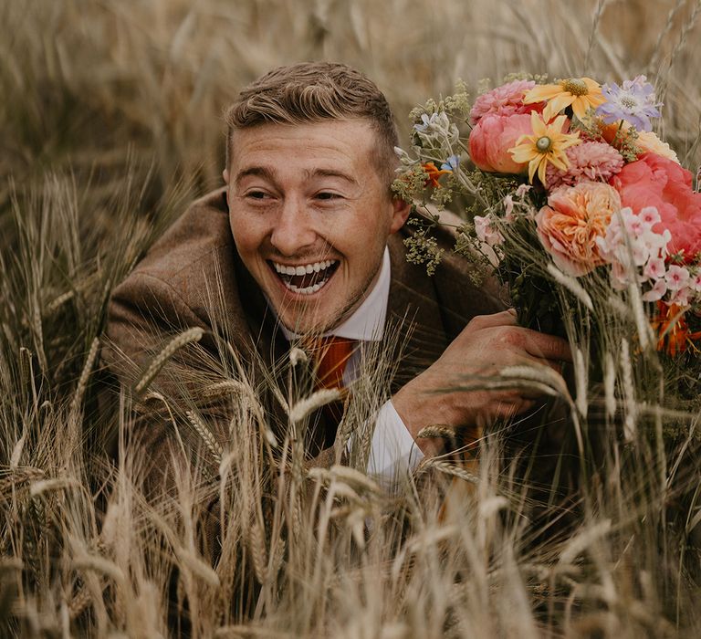 Groom is goofy in the fields posing with the bridal bouquet