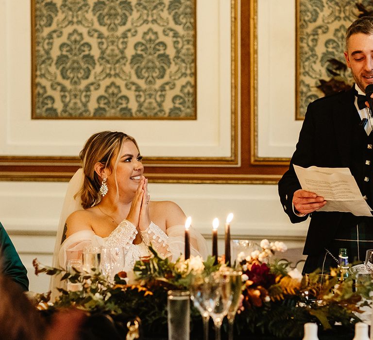 Bride with sparkly earrings puts her hands together for speech 