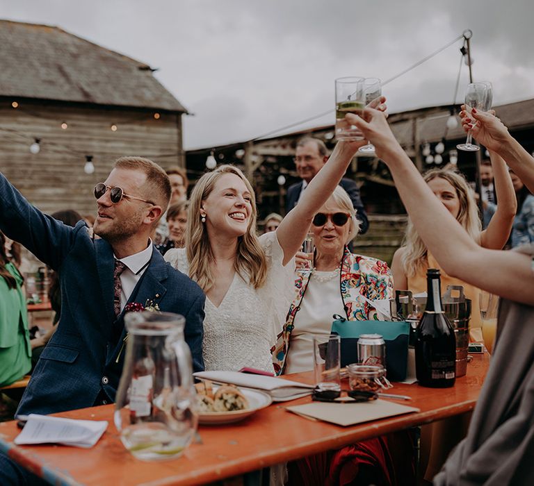 Bride and groom in sunglasses and guests all raise their glass in a toast for the couple