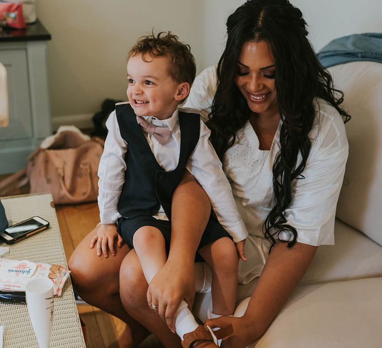 Bride puts on your page boy's shoes as he wears a dark grey waistcoat and pink bow tie