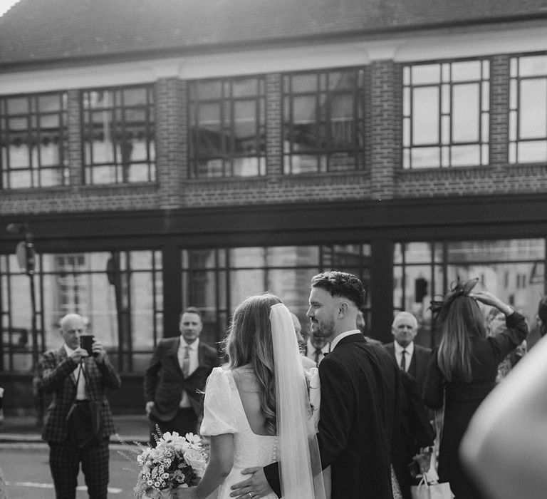 Groom in black tie puts his arm around the bride as they exit their ceremony with bride in button details puff sleeve wedding dress