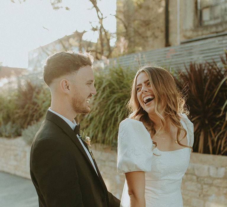 Groom in black tie laughs and smiles with the bride in puff sleeve patterned wedding dress after their registry office wedding