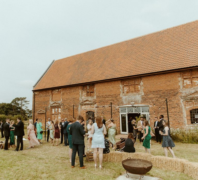 Wedding guests socialise outside of Godwick Barn wedding venue 