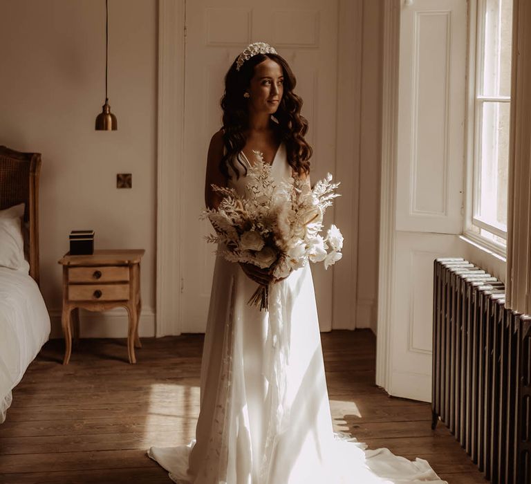 Bride with curled brown hair wearing a flower bridal headband and carrying a white orchid and dried flower wedding bouquet