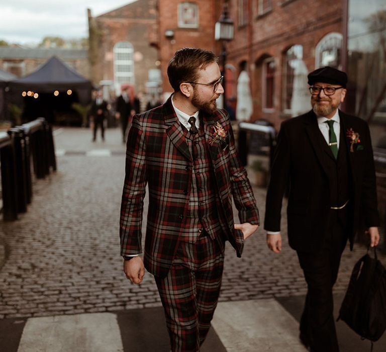 Groom walks down cobbled street wearing bespoke tartan suit on his wedding day