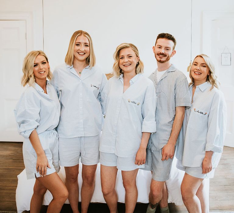 Bride stands with her bridesmaids and Man of Honour who wearing matching embroidered pyjamas in light blue 