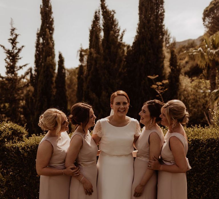 Bride stands with her bridesmaids who wear pale pink dresses complete with capped sleeves 