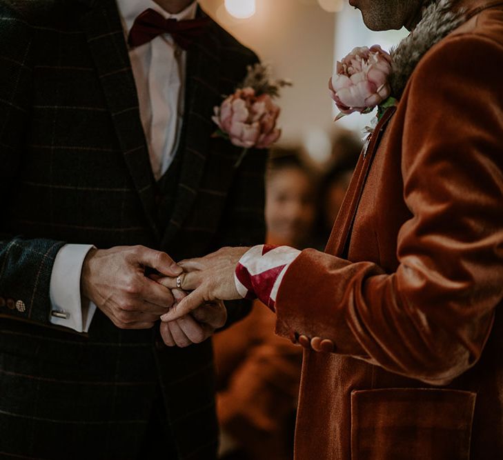 Groom places ring on his grooms hand during wedding ceremony 