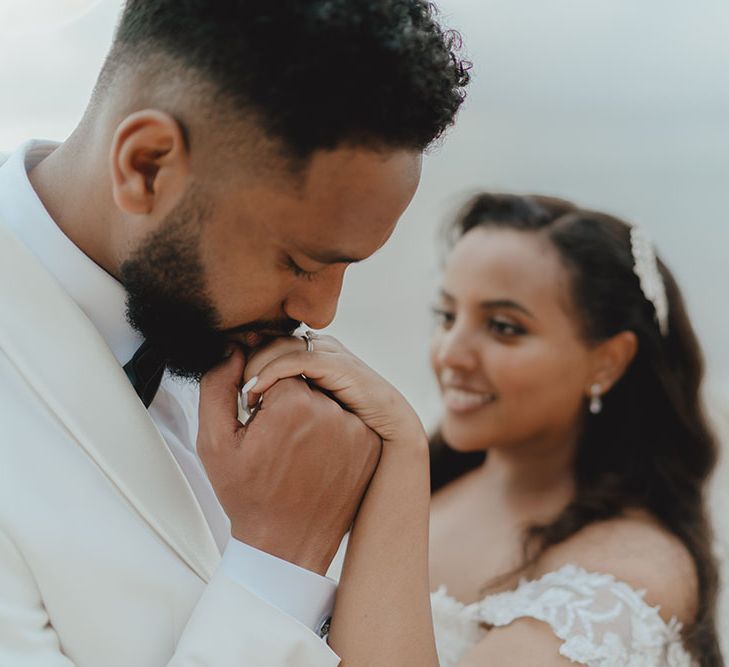 Groom kisses his wife's hand on their wedding day as they stand at the sea front in Phuket 