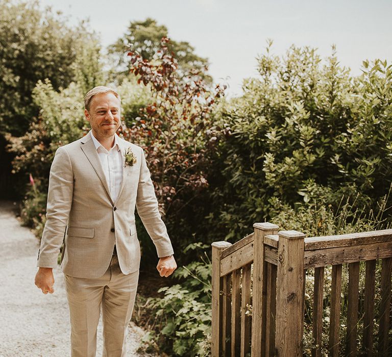 Guest in a pale wedding suit smiling as he gets the first look at the bride 