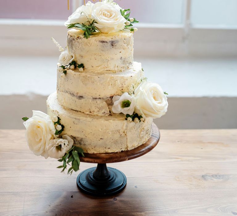 Three-tier naked wedding cake complete with white rose flower decor and gold cake topper 