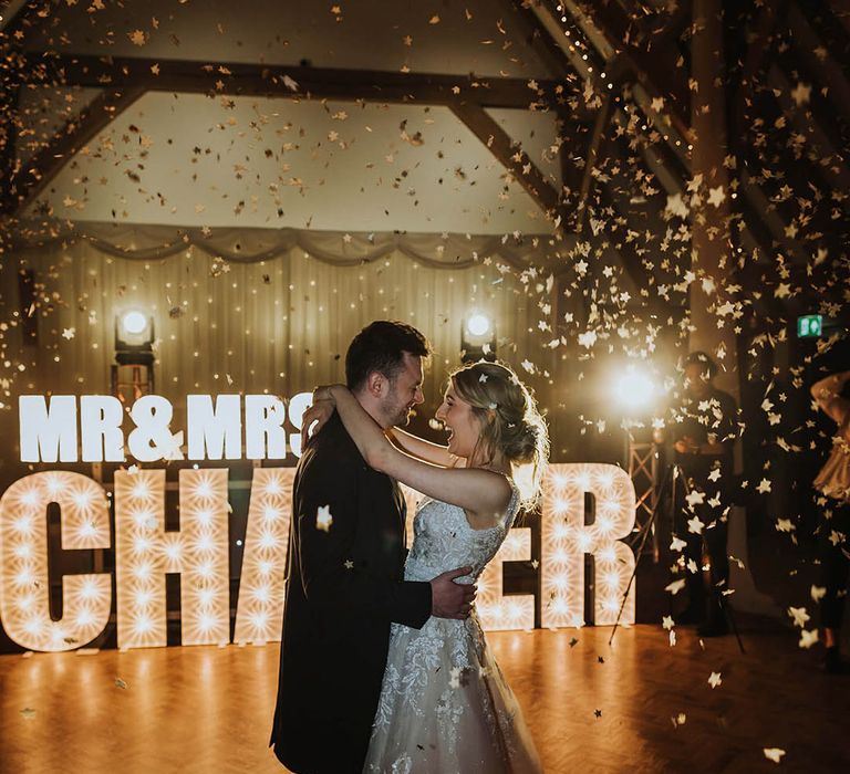 Bride and groom share their first dance in front of letter lights spelling out their new married name 