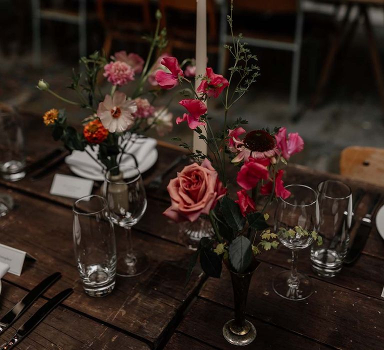 Long tapered ivory dinner candle in clear candle holder on minimal neutral wedding tablescape with pops of colourful floral decorations