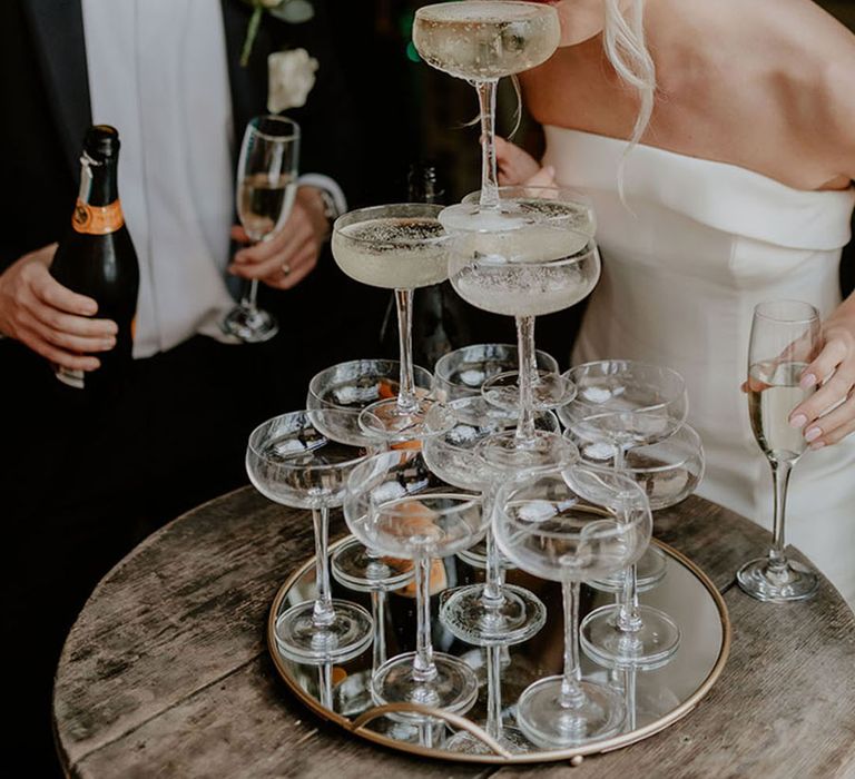 Bride in a strapless wedding dress takes a sip from a champagne tower 