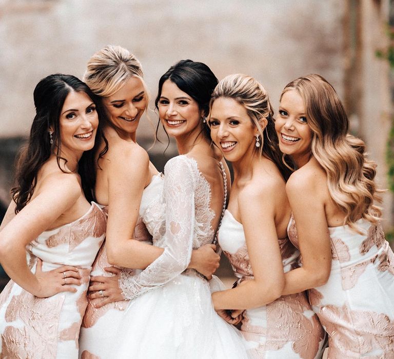 The bridesmaids in sweetheart strapless white dresses with a rose gold pattern with the bride 