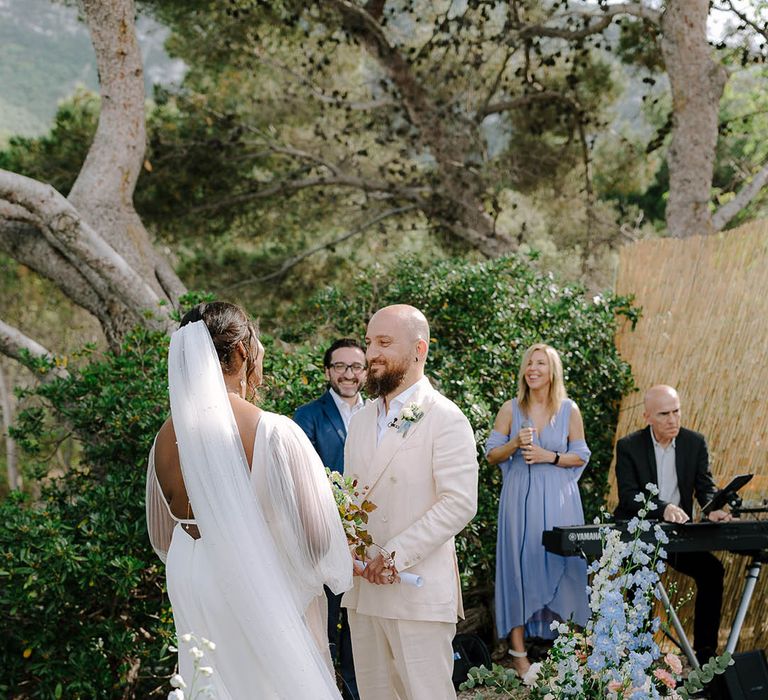 Bride and Groom smiling at each other at the alter surrounded by beautiful blue flowers