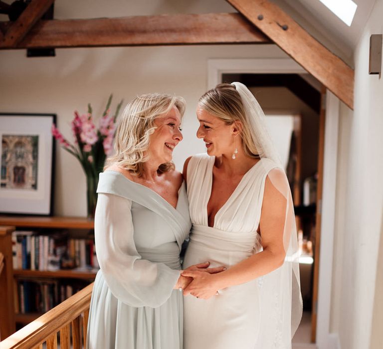 Mother of the bride in a sage green dress smiles at the bride as they get ready for the wedding 