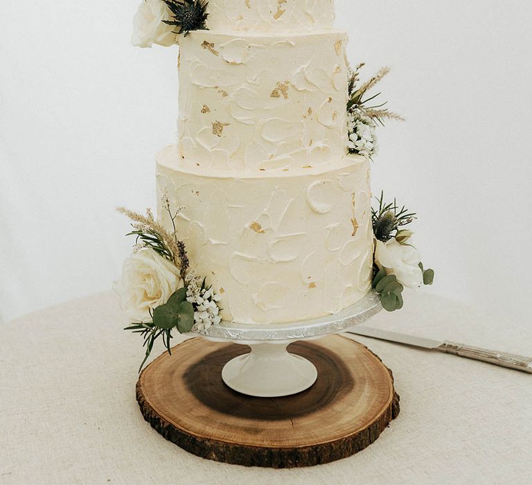 Three tier white frosted wedding cake complete with gold leaf and floral decor 