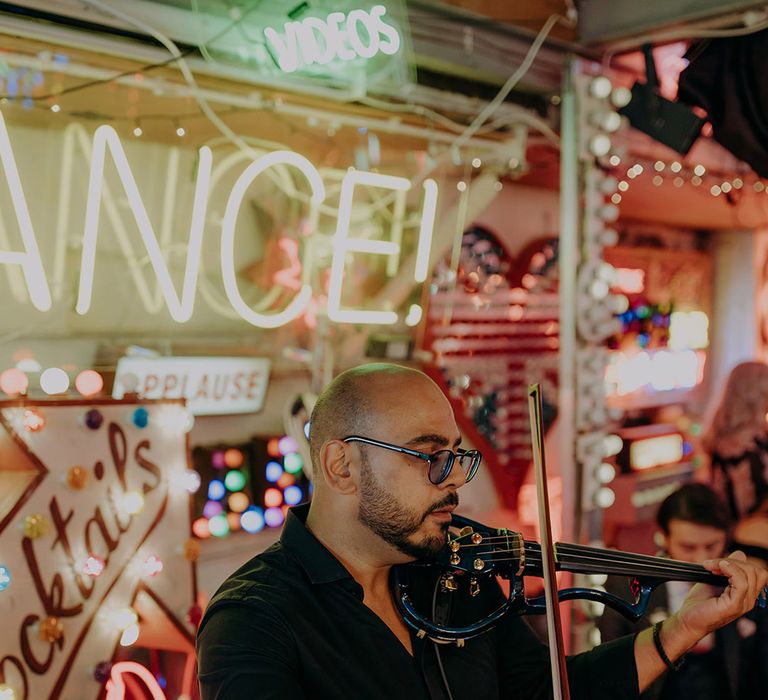 Live wedding music; electric violinist wedding entertainment with neon signs in the background at London wedding 