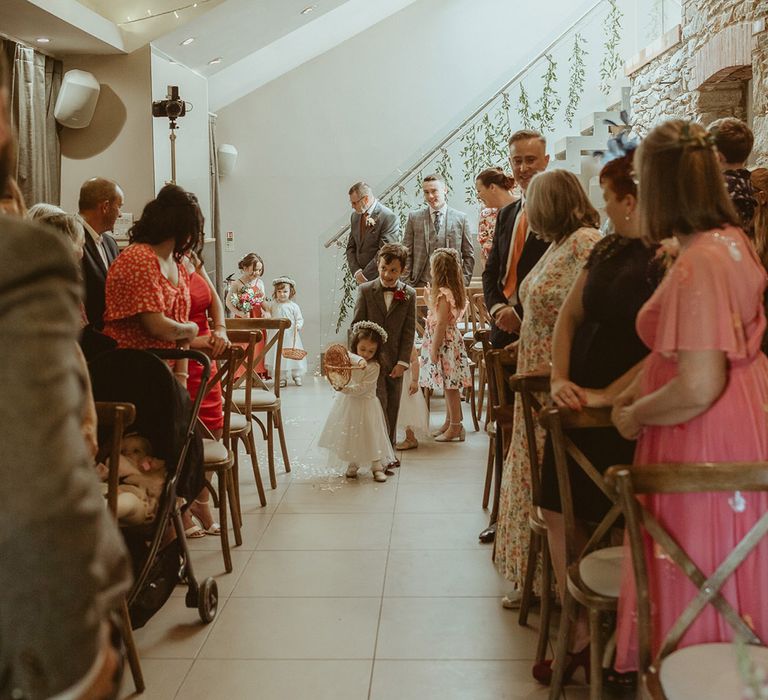 Wedding guests stand as the flower girl empties the wicker basket of white petals walking with other children a part of the wedding ceremony 