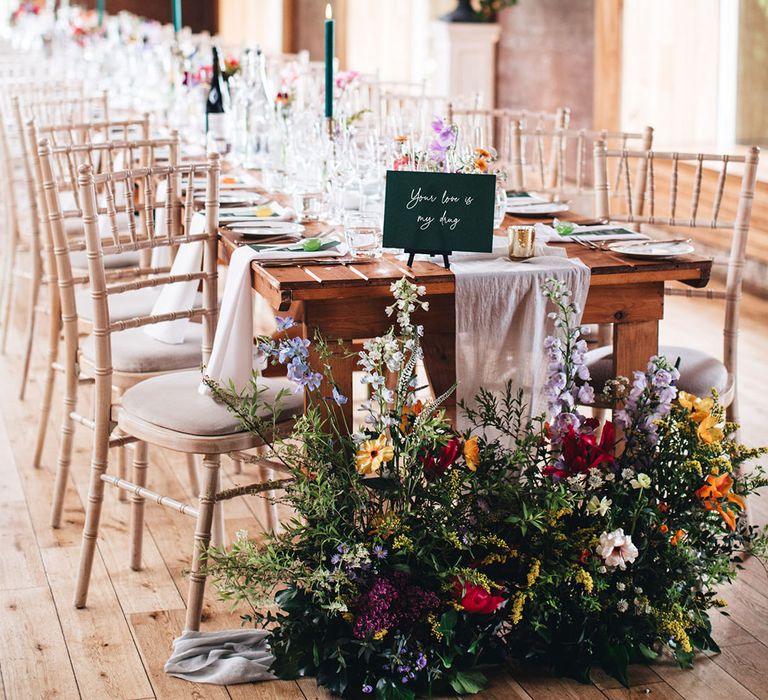 Lilac, yellow, red, and pink wedding wildflowers decorate the ends of the long banquet reception tables with green table name signs 