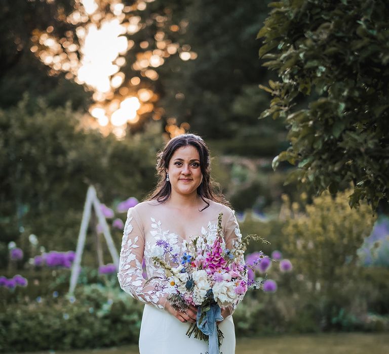 Illusion lace wedding dress with subtle mermaid skirt holding colourful bouquet of flowers 