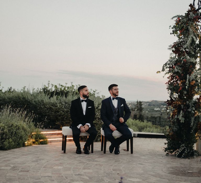 Two grooms in black and sexy tuxedos at outdoor wedding ceremony 