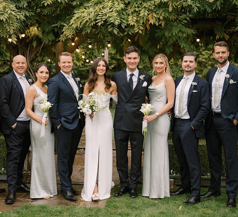 Bridesmaids in sage green satin bridesmaid dresses with the groom and the groomsmen wear sage green ties to match with white flower buttonhole