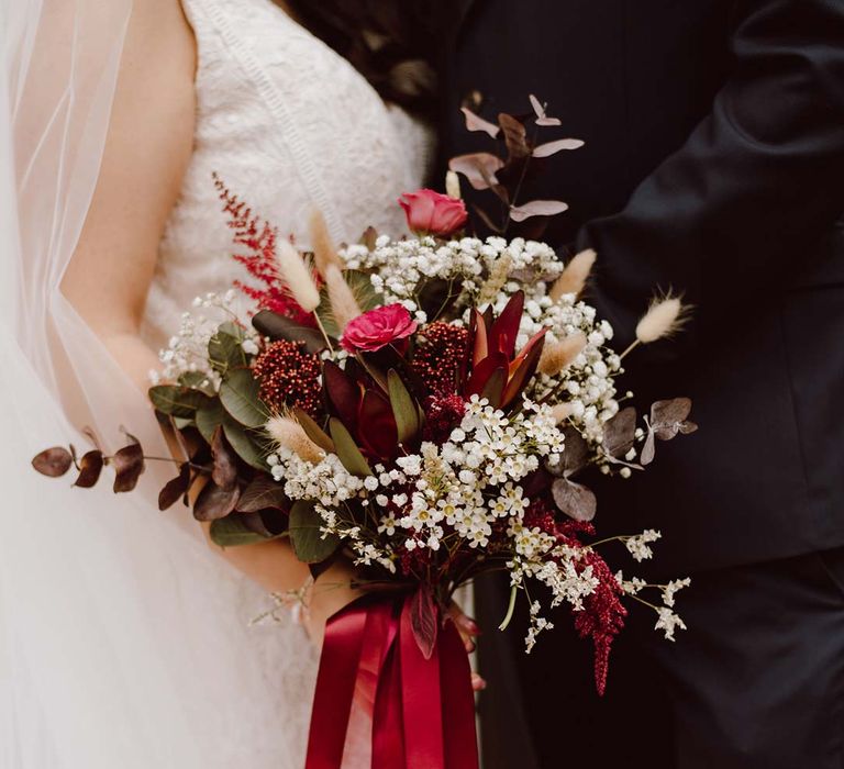 Bride holding red garden rose, red dried flower, eucalyptus, pampas grass and baby's-breath bridal bouquet with red ribbon