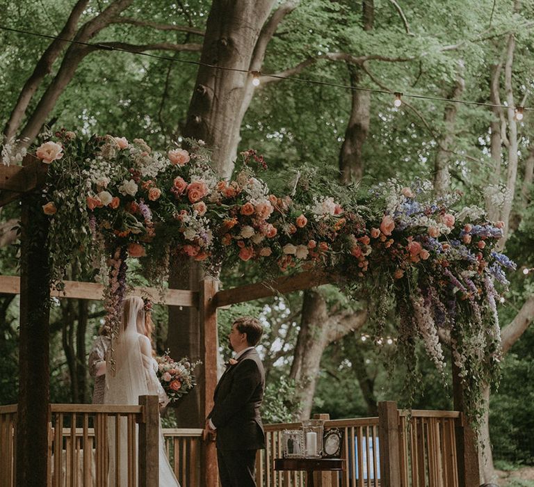 Outdoor woodland wedding with colourful pink, purple and white wedding flower altar decoration 