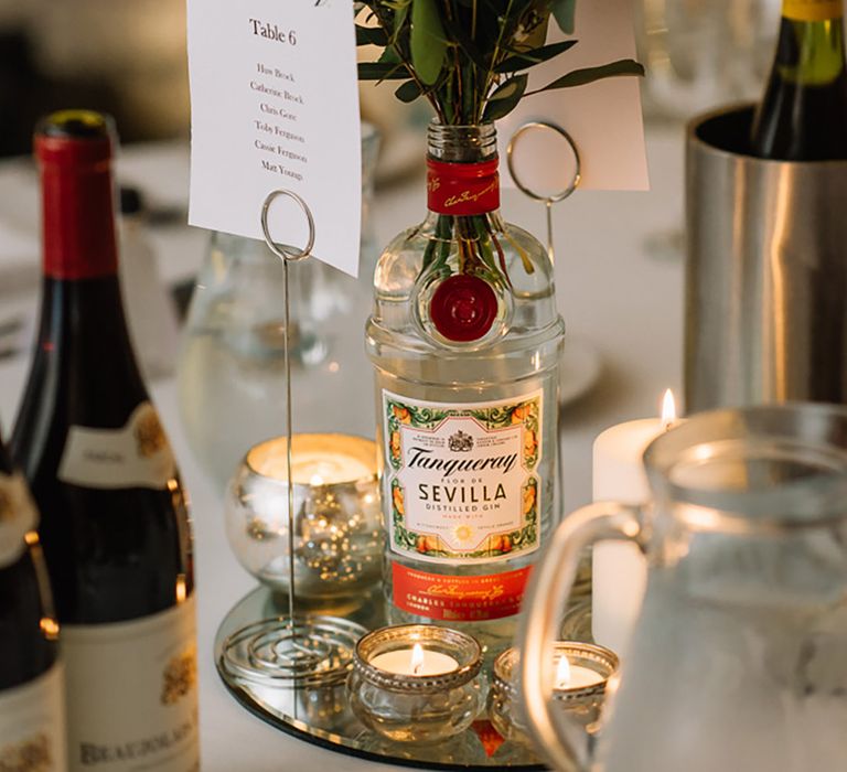 Mirrored tray holding an empty bottle of gin with the wedding tables named after different alcohol 