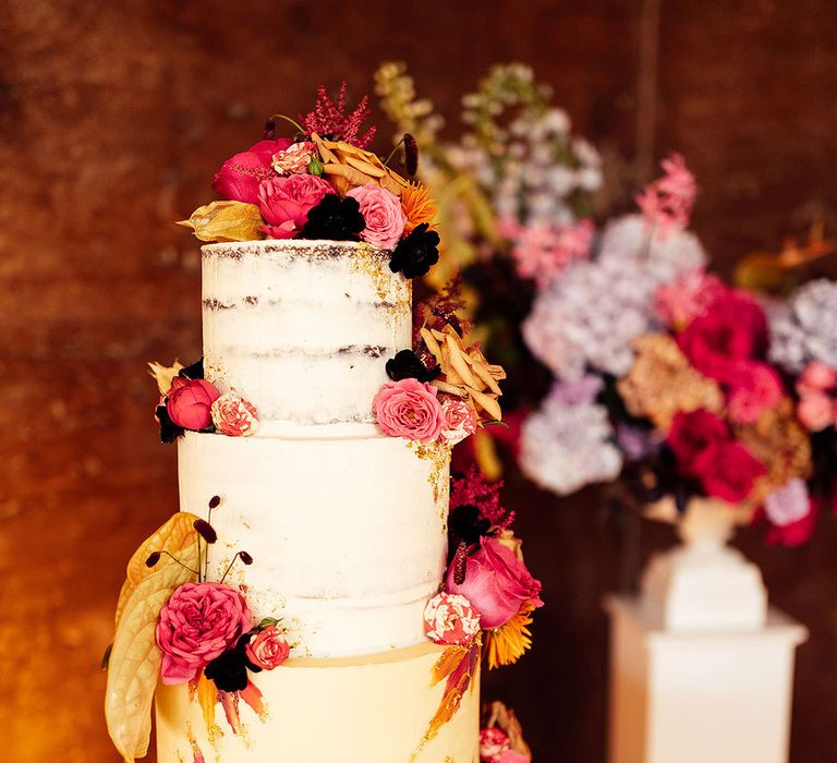 Three tier semi-naked rustic wedding cake with gold flakes and pink wedding cake decorations 