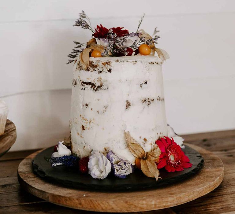 Single tier semi-naked wedding cake with edible dried flowers on wooden slate 