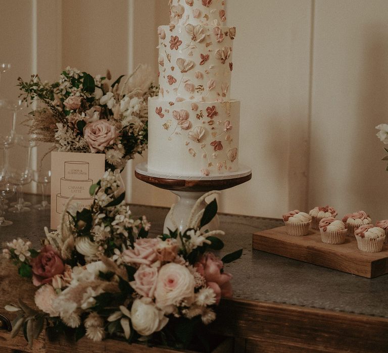 Three tier white frosted wedding cake with light pink and dark pink flower icing 