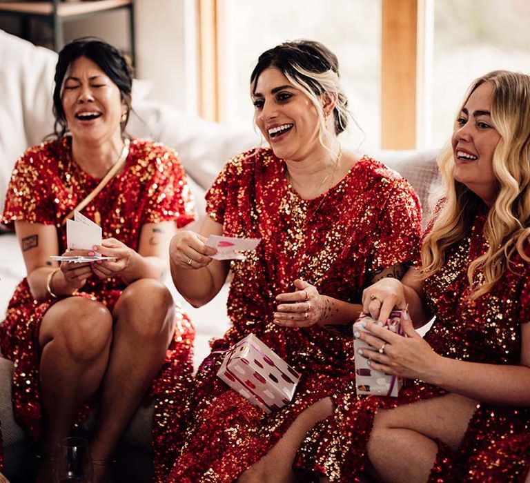 Bridesmaids getting ready for the wedding and opening presents in red sequin bridesmaid dresses 