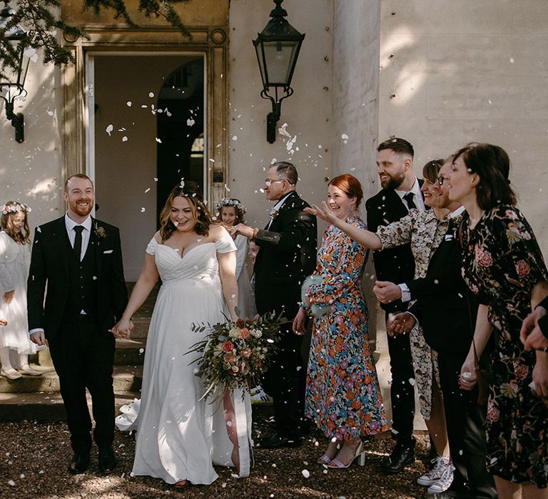 Groom in black and white wedding suit walking out of the humanist ceremony with the bride to white confetti exit 