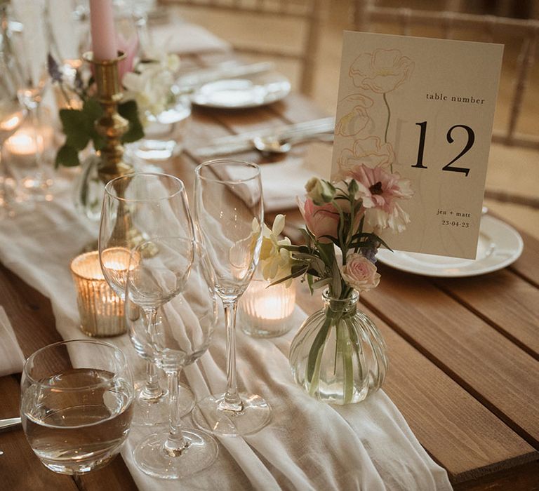 Pretty floral table number sign with small pink bud vases with draped table runner and pink wedding candles 